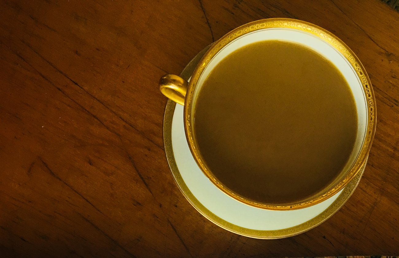 A gilt-rimmed teacup and saucer on a dark wood table