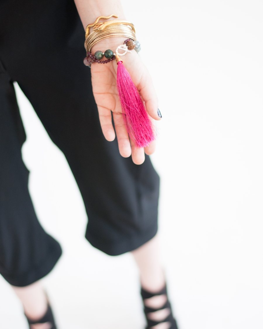 Kellie Adkins in black, wearing stacked gold bangles and a beaded bracelet with a bright pink tassel